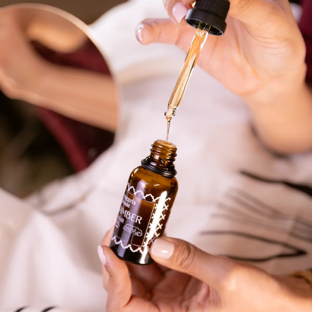 Geöffnete Amber-Haarölflasche mit Pipette in den Händen einer Person