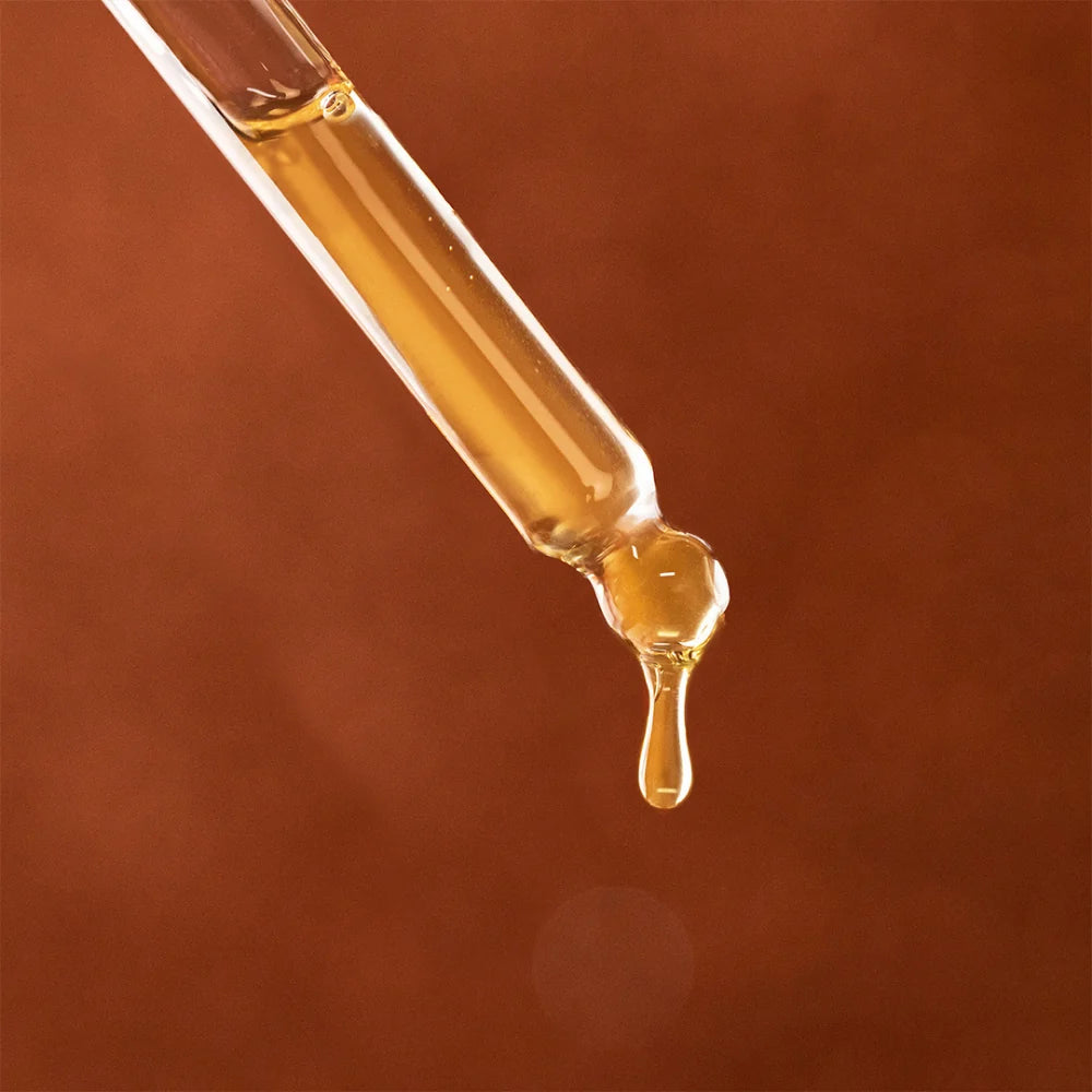 Pipette mit goldfarbenem Nuggela & Sulé Amber Haaröl vor braunem Hintergrund